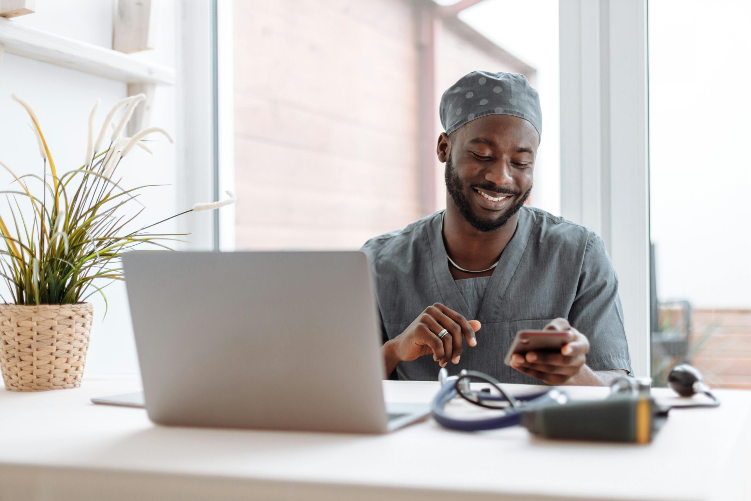 pexels-photo-5327914-5327914-2 Smiling healthcare professional using phone in office with laptop and medical tools.